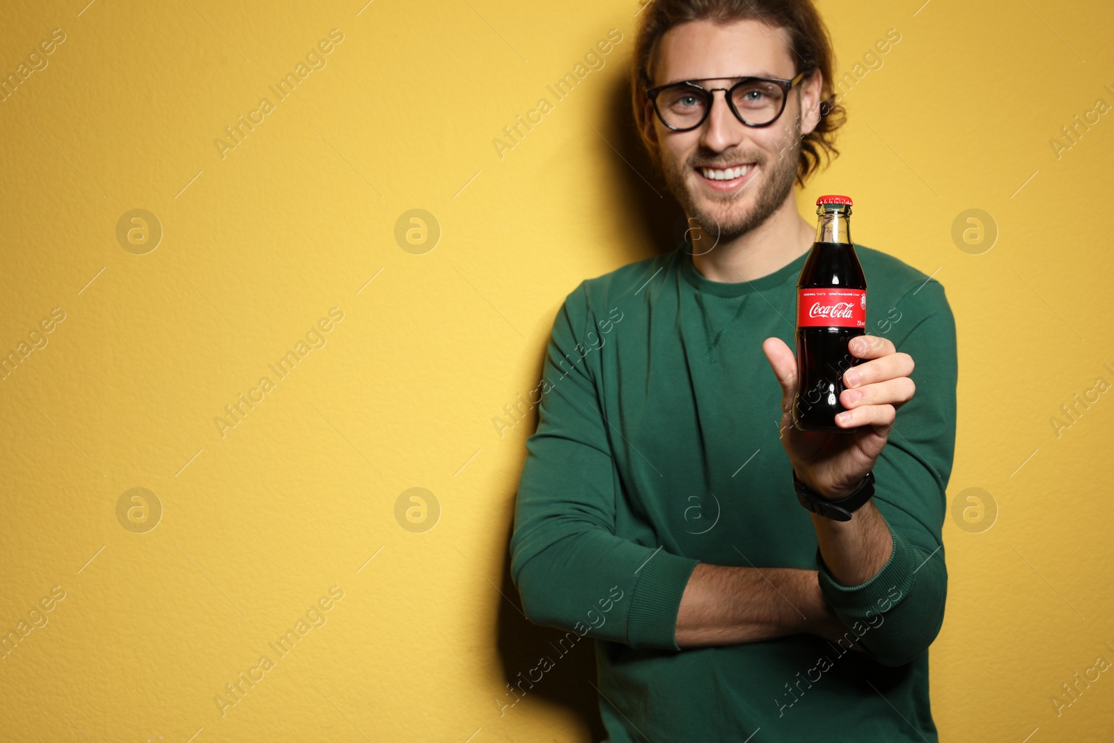 Photo of MYKOLAIV, UKRAINE - NOVEMBER 28, 2018: Young man with bottle of Coca-Cola on color background, space for text