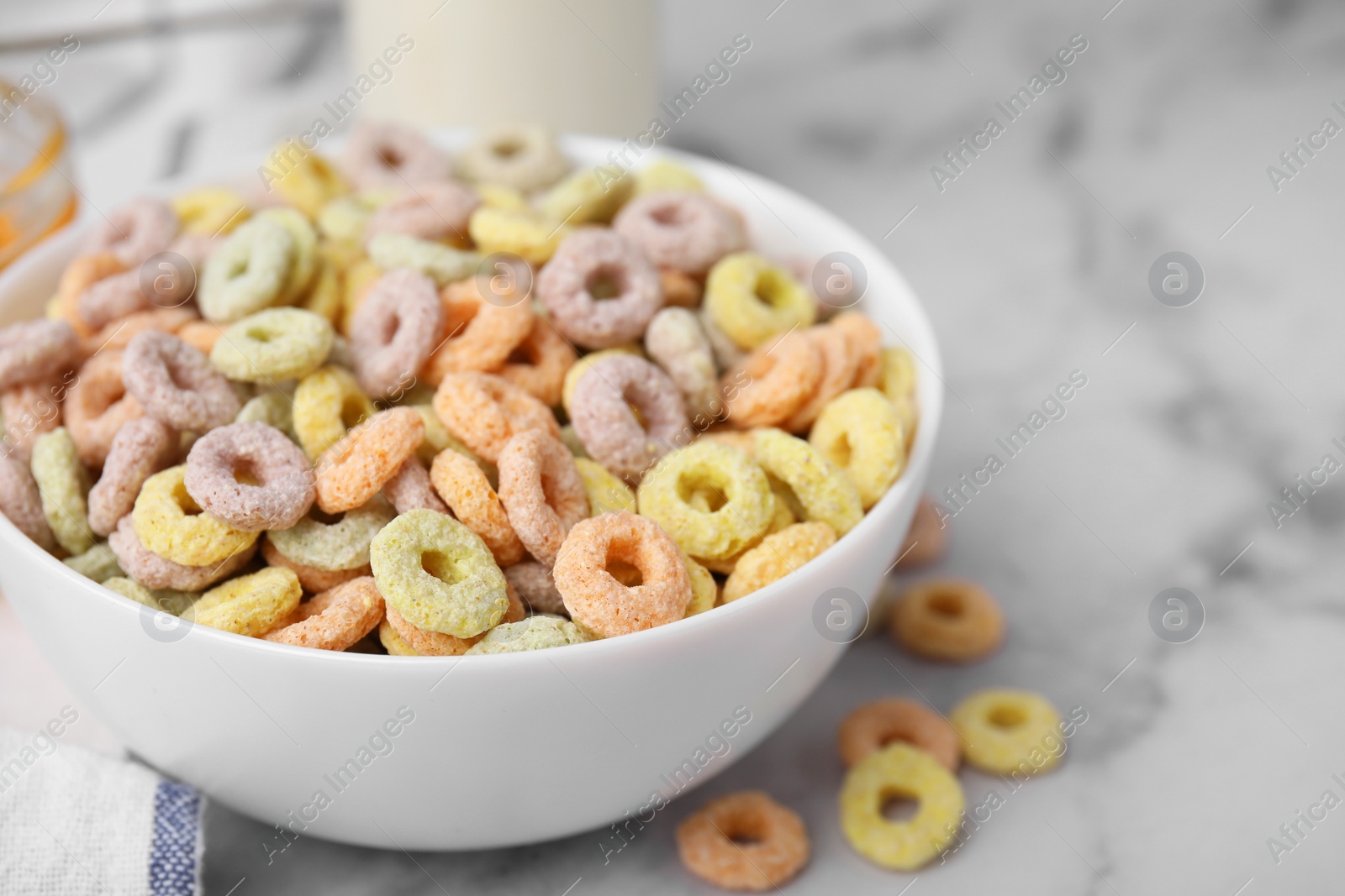 Photo of Tasty cereal rings in bowl on white marble table, closeup. Space for text