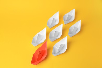 Photo of Group of paper boats following orange one on yellow background. Leadership concept