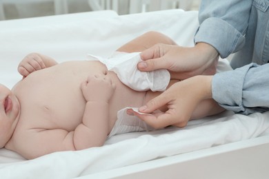 Mother changing baby's diaper on table at home, closeup