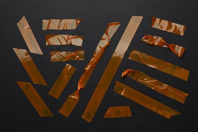 Photo of Many pieces of orange adhesive tape on black background, flat lay