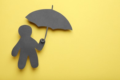 Photo of Black paper cutout of human holding umbrella on yellow background, top view with space for text. Depression concept