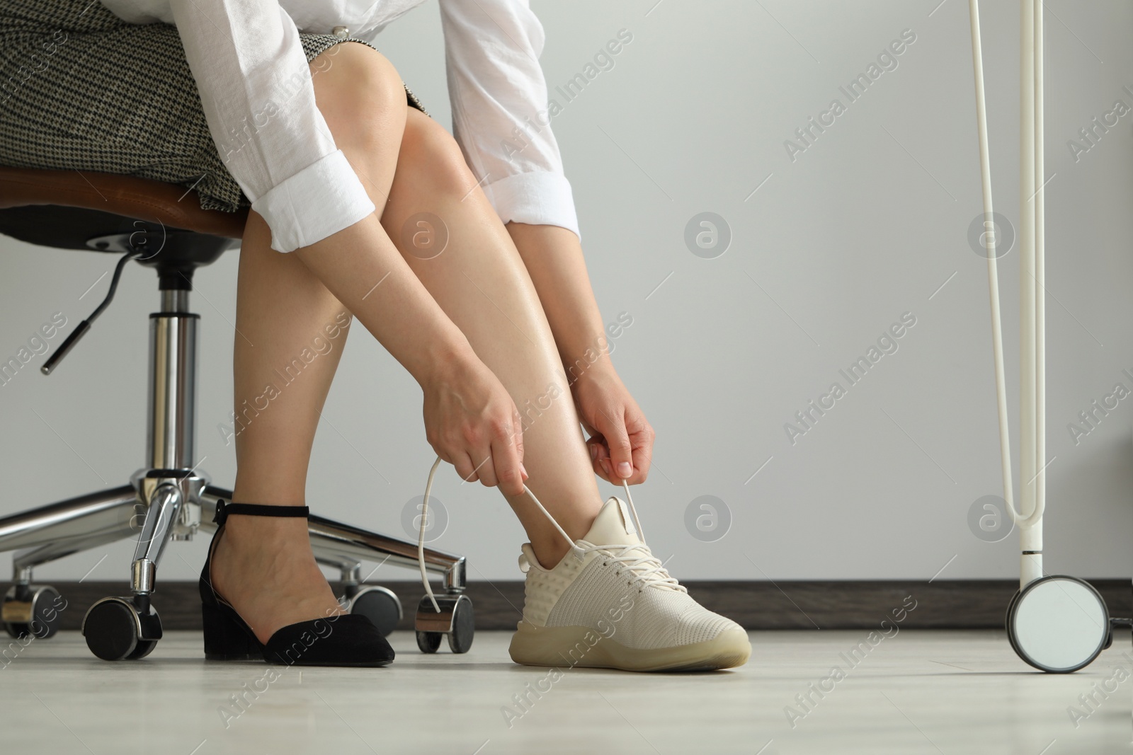 Photo of Woman taking off uncomfortable shoes and putting on sneakers in office, closeup
