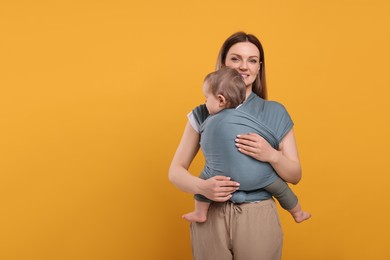 Photo of Mother holding her child in baby wrap on orange background. Space for text