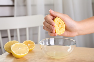 Woman squeezing lemon juice into glass bowl at wooden table, closeup