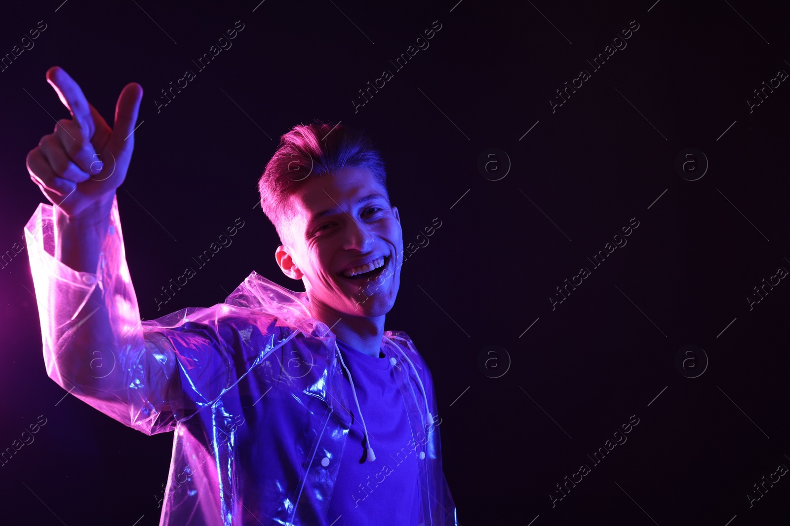 Photo of Young man wearing clear coat on dark background in neon lights. Space for text