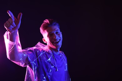 Young man wearing clear coat on dark background in neon lights. Space for text