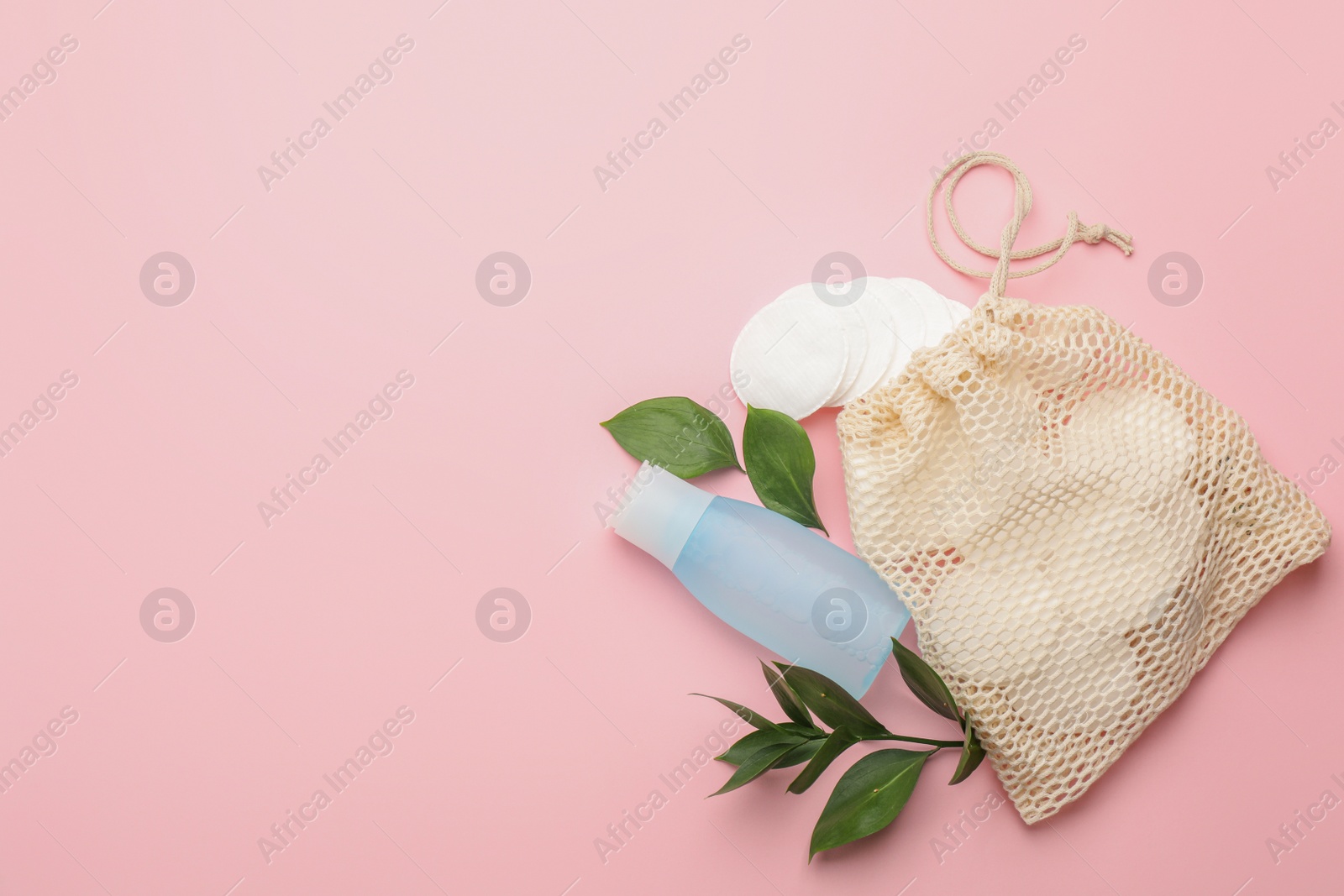 Photo of Cotton pads, leaves, sack and makeup removal product on pink background, flat lay. Space for text