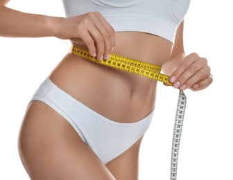Photo of Young woman measuring waist with tape on white background, closeup