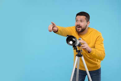 Photo of Happy astronomer with telescope pointing at something on light blue background. Space for text