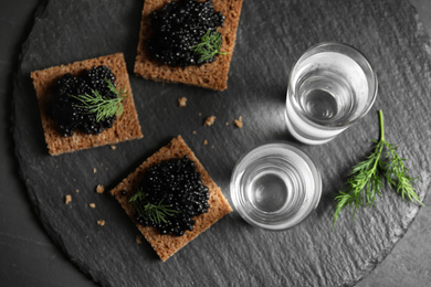 Photo of Cold Russian vodka with snacks on black table, flat lay