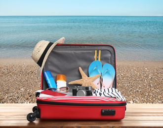 Image of Suitcase with different beach objects on wooden table near sea