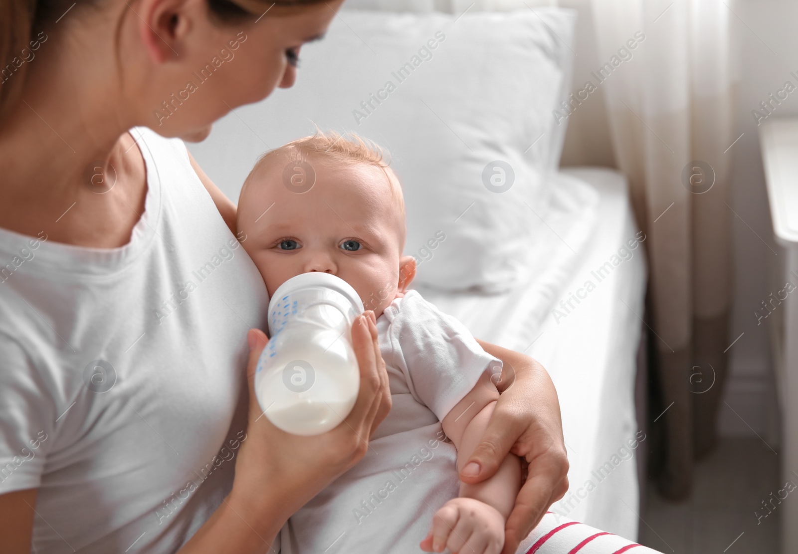 Photo of Lovely mother holding and feeding her baby from bottle on bed. Space for text