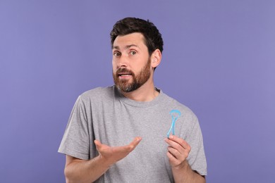 Photo of Confused man with tongue cleaner on violet background