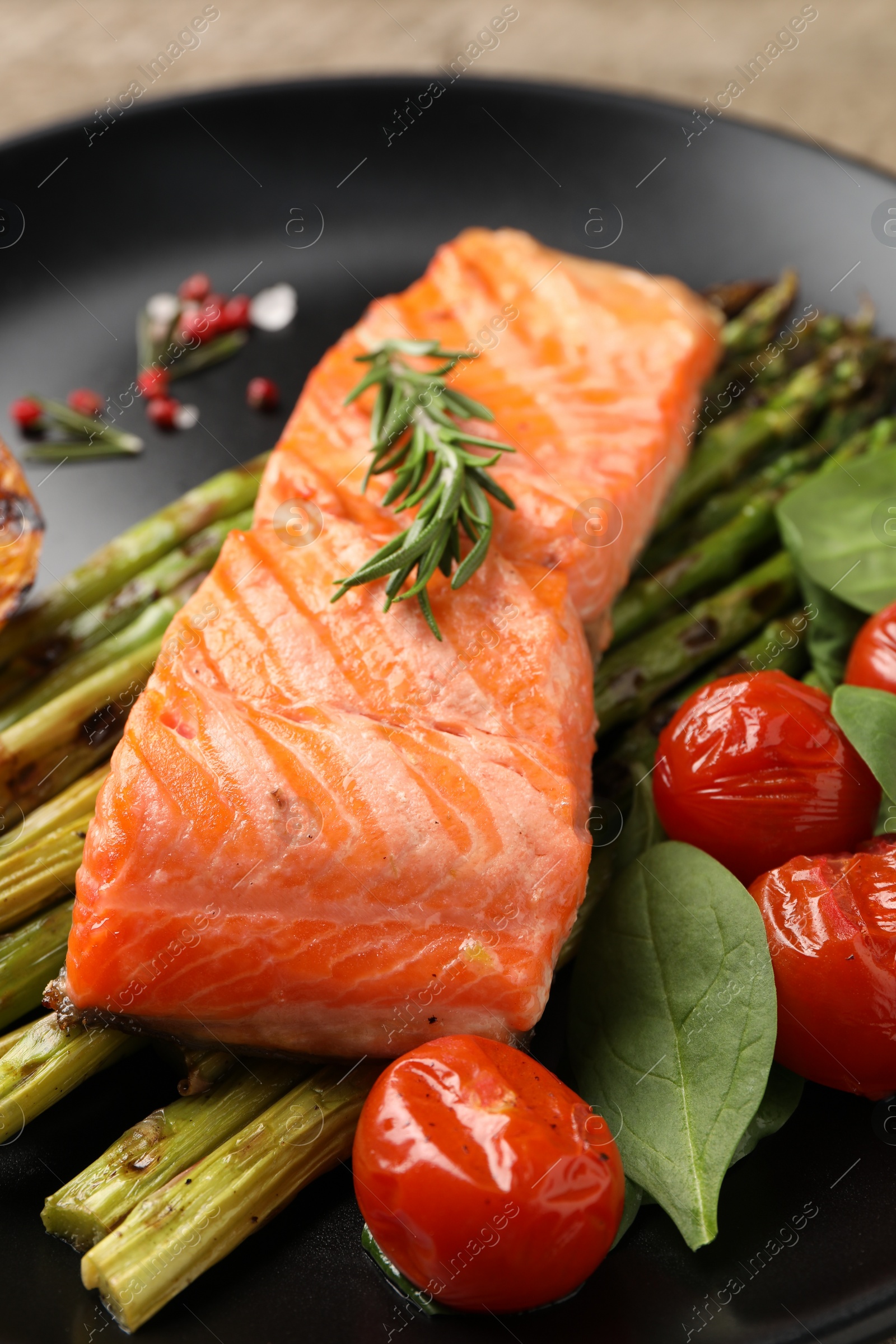 Photo of Tasty grilled salmon with tomatoes, asparagus, spices on plate, closeup