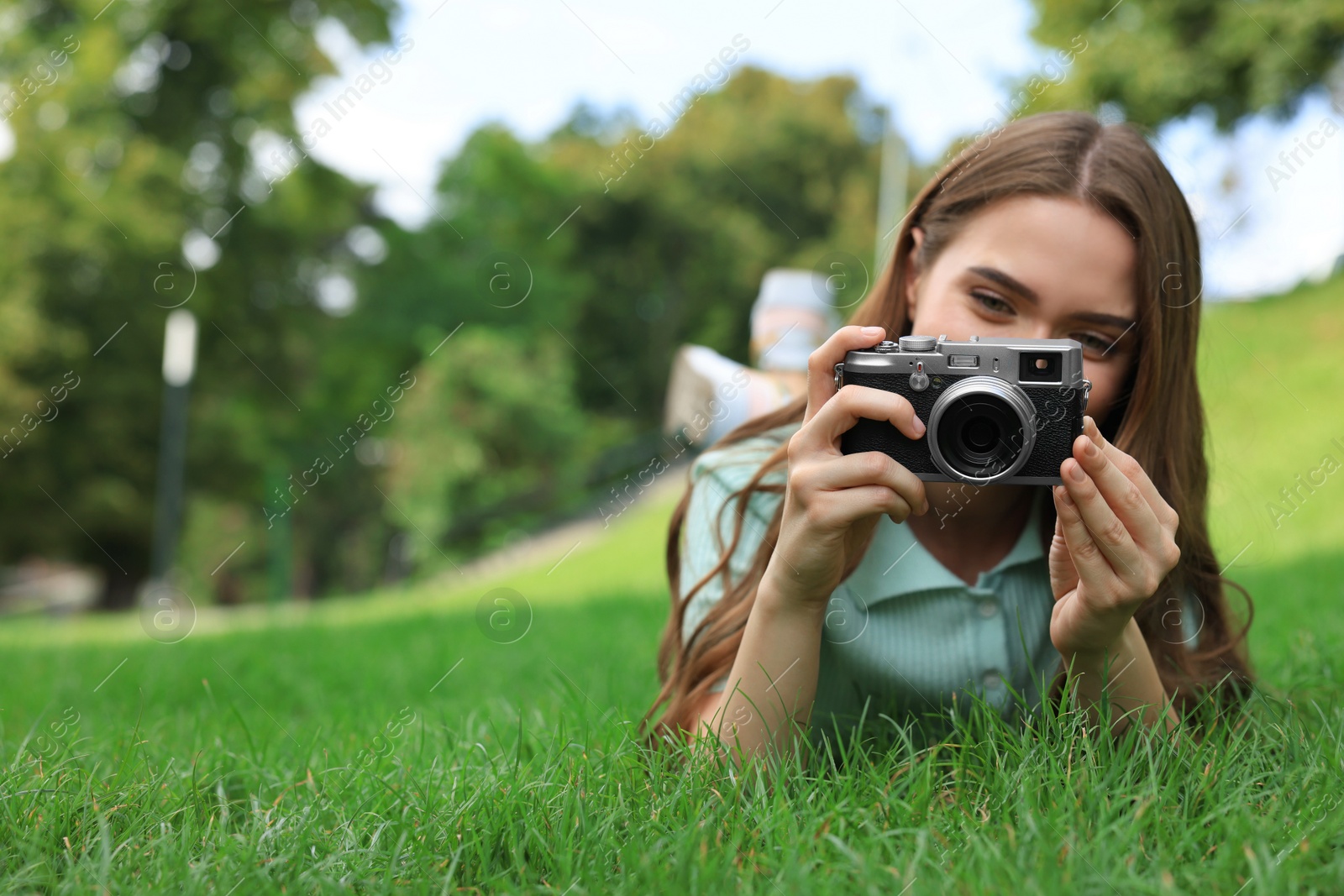 Photo of Young woman with camera taking photo on green grass outdoors, space for text. Interesting hobby