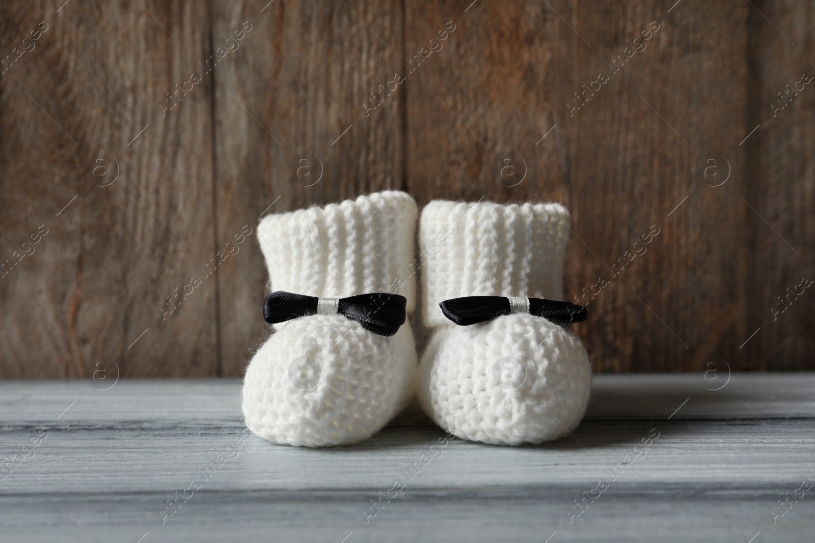Photo of Handmade baby booties on table against wooden background