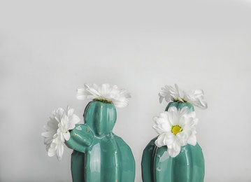 Trendy cactus shaped vases with flowers against light wall. Creative decor