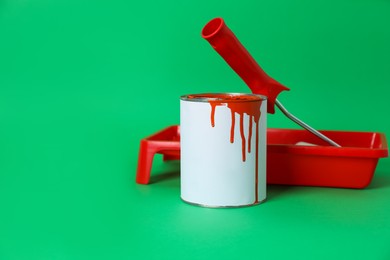 Photo of Can of orange paint, roller brush and container on green background. Space for text