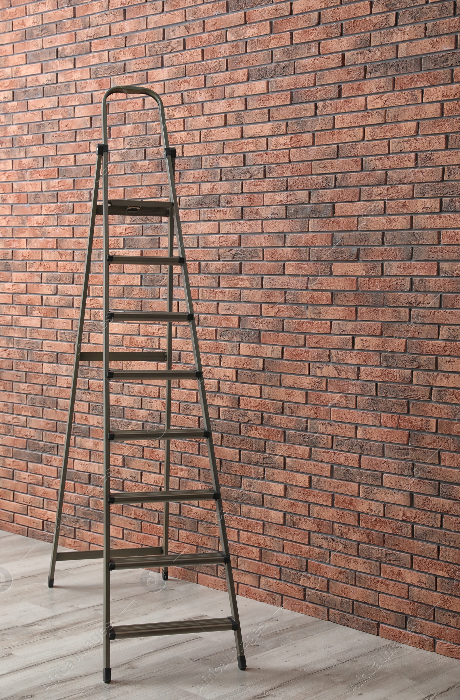 Photo of Metal stepladder near brick wall indoors. Construction tool