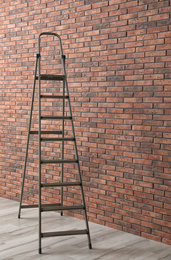 Metal stepladder near brick wall indoors. Construction tool