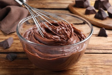 Whipping chocolate cream with balloon whisk on wooden table, closeup