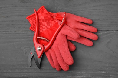 Pair of red gardening gloves and secateurs on grey wooden table, top view