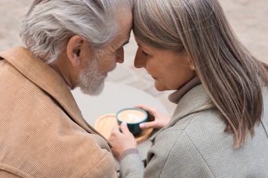 Photo of Portrait of affectionate senior couple drinking coffee at table outdoors, closeup