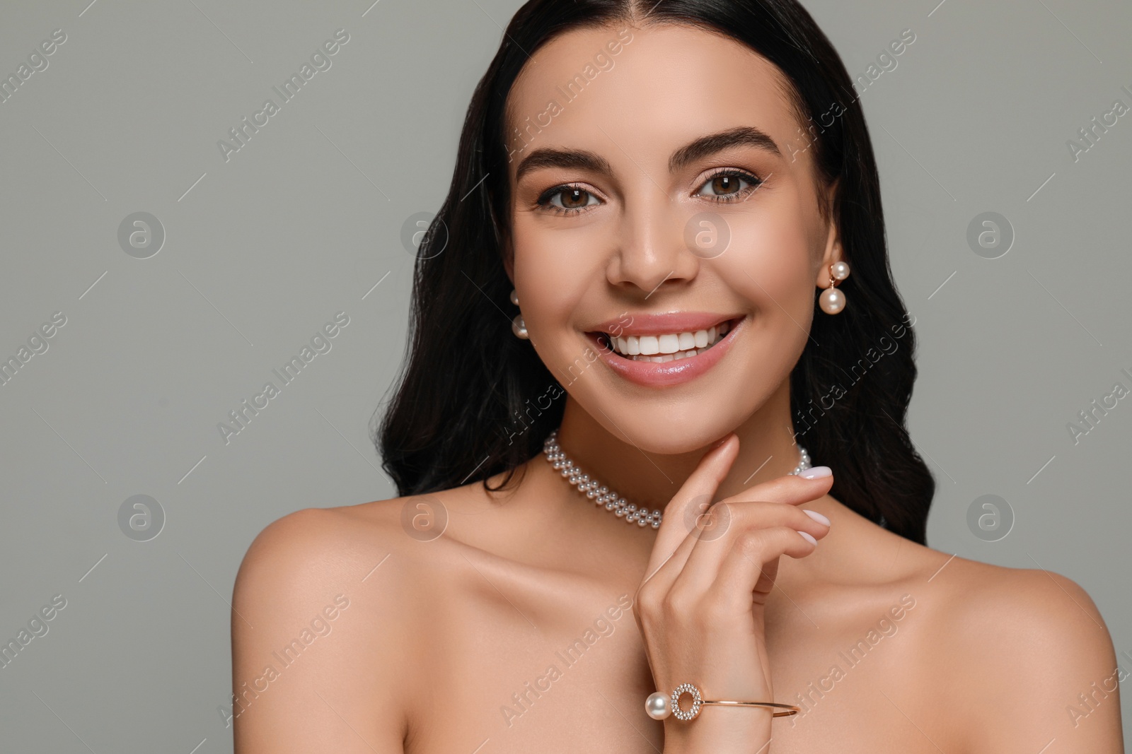 Photo of Young woman wearing elegant pearl jewelry on grey background