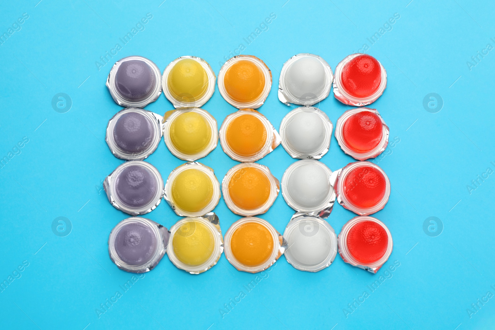 Photo of Tasty bright jelly cups on light blue background, flat lay