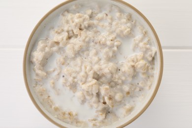 Photo of Tasty boiled oatmeal in bowl on white wooden table, top view