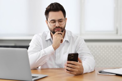 Photo of Young man using smartphone at wooden table in office