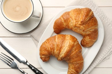 Delicious fresh croissants served with coffee on white wooden table, flat lay