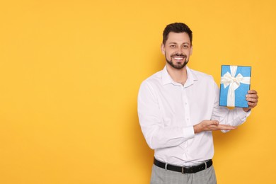 Photo of Happy man with gift box on yellow background, space for text