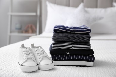 Photo of Stack of baby boy's clothes and shoes on bed at home