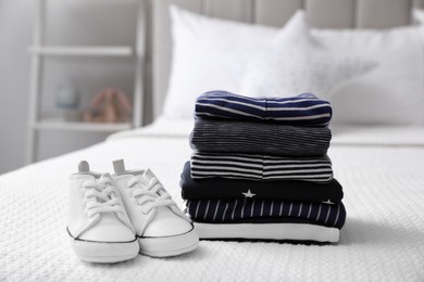 Stack of baby boy's clothes and shoes on bed at home