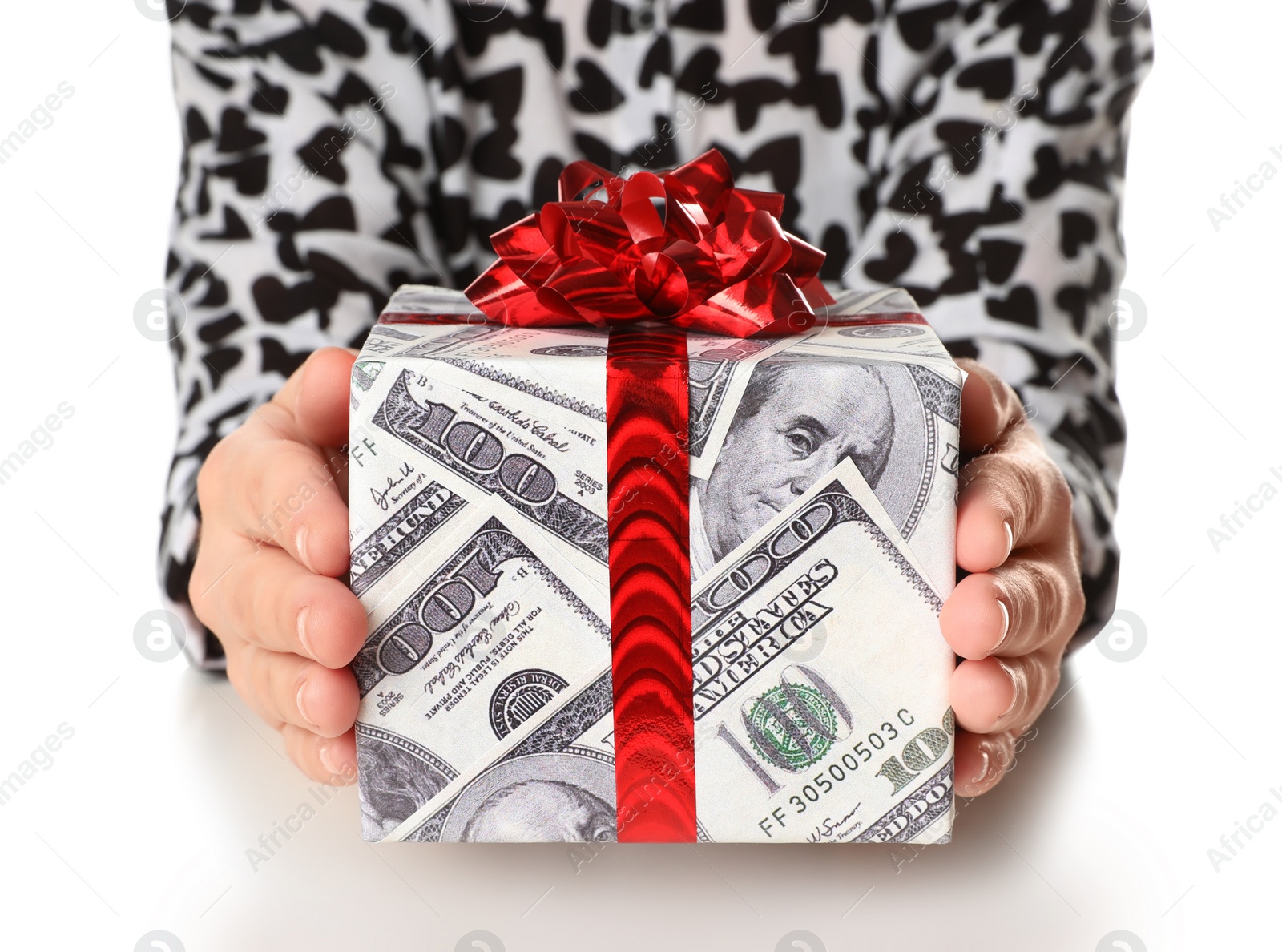 Photo of Woman holding gift box wrapped in decorative paper with dollar pattern on white background, closeup