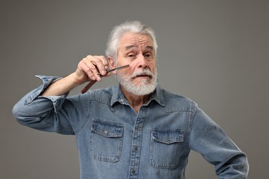 Senior man shaving beard with blade on grey background