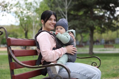 Photo of Mother holding her child in sling (baby carrier) on bench in park