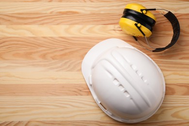 Photo of Safety equipment. Hard hat and protective headphones on wooden background, flat lay. Space for text