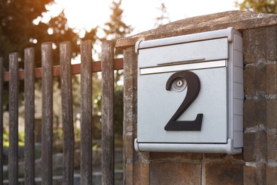 Photo of Metal mailbox with number 2 on stone fence near wooden gate outdoors, space for text