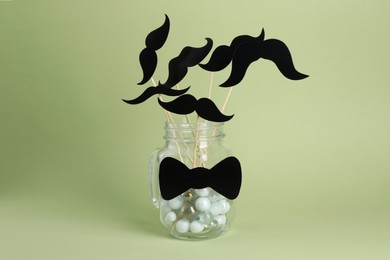 Fake paper mustaches on sticks in jar with bow tie against pale green background
