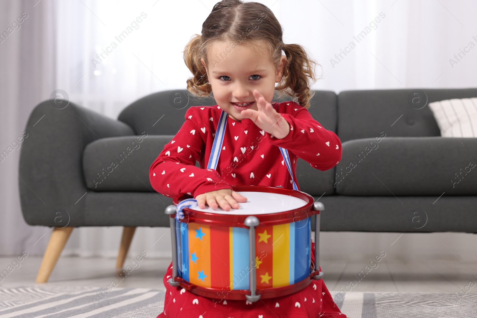 Photo of Little girl playing toy drum at home