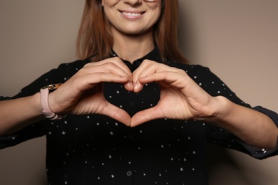 Woman showing HEART gesture in sign language on color background, closeup