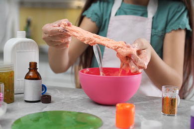 Photo of Little girl kneading DIY slime toy at table indoors, closeup