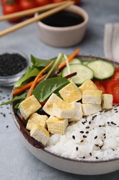 Delicious poke bowl with vegetables, tofu and mesclun on light grey table
