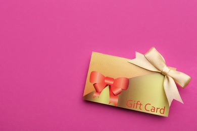 Photo of Gift card with bow on pink background, top view. Space for text