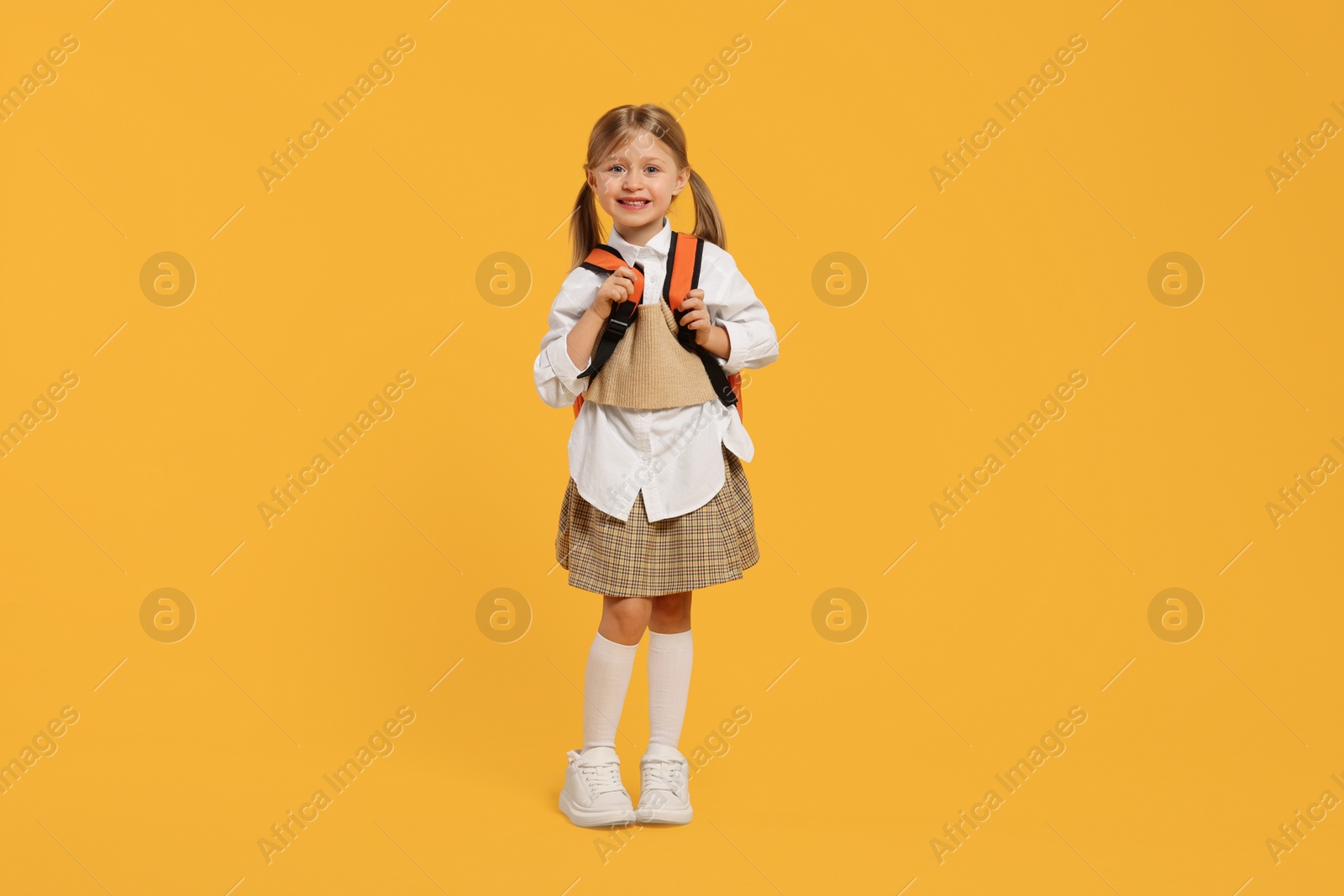 Photo of Happy schoolgirl with backpack on orange background