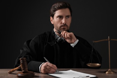 Photo of Judge working with papers at wooden table against black background