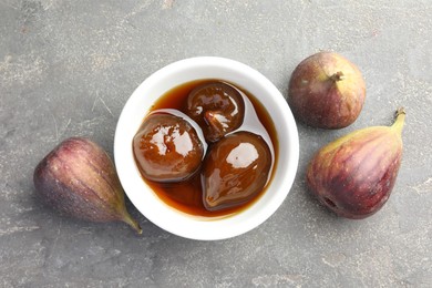 Photo of Bowl of tasty sweet jam and fresh figs on grey table